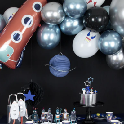 Decoração temática espacial com balões, foguetes e miniaturas de robôs sobre mesa