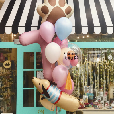 Balões coloridos festivos em frente a loja com porta azul e toldo riscado preto e branco