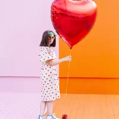 Criança com vestido de bolinhas em skate segurando balão em forma de coração