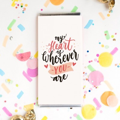 Barra de chocolate com capa branca e texto colorido, rodeada por confetes coloridos