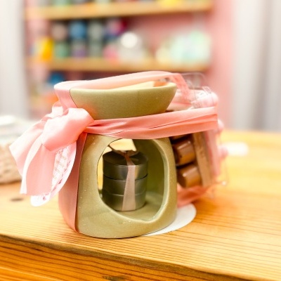 Conjunto de difusor em cerâmica verde com fita rosa e velas aromáticas em embalagem transparente sobre mesa de madeira