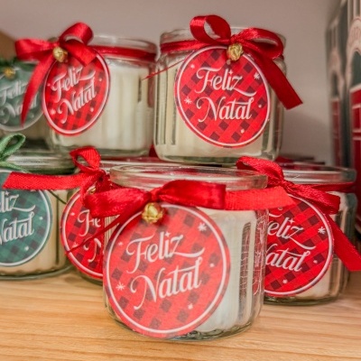 Velas em frascos de vidro com etiquetas 'Feliz Natal' e fitas vermelhas