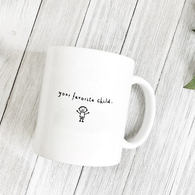 Caneca branca com frase e desenho, sobre superfície de madeira clara