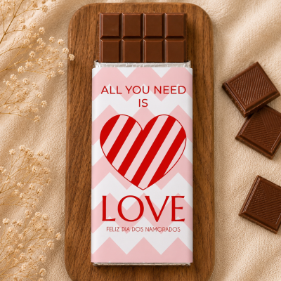 Barra de chocolate com embalagem rosa e branca com coração e texto sobre prato de madeira
