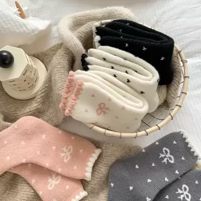 Meias infantis de várias cores com padrões de corações e laços, numa cesta sobre uma cama branca