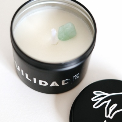 Vela branca em recipiente preto com tampa ao lado e desenho branco de mão