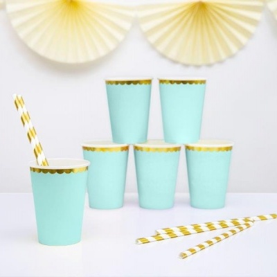 Seis copos descartáveis azul claro com borda dourada e canudos brancos com riscas douradas sobre superfície branca