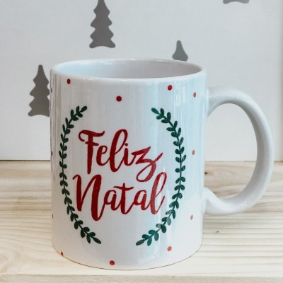 Caneca branca com texto 'Feliz Natal' e decoração verde e vermelha