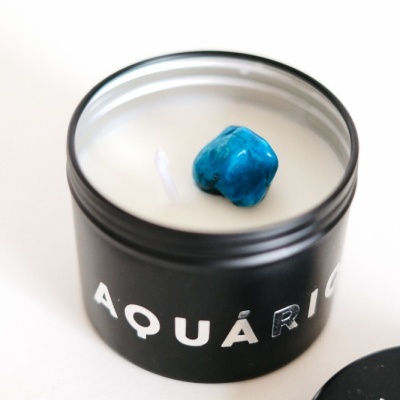 Vela branca em recipiente preto com pedra azul e texto AQUÁRIO