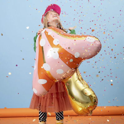 Menina com balão metálico em forma de cogumelo rodeada de confetes
