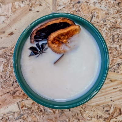 Vela branca em recipiente verde com decoração de casca seca e anis