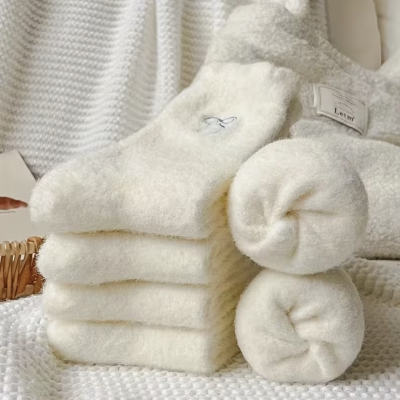 Meias felpudas brancas empilhadas e enroladas sobre tecido texturizado branco