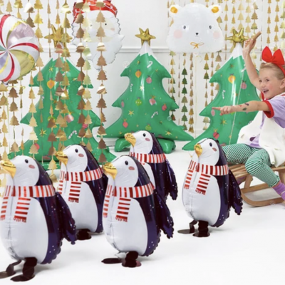 Pinguins insufláveis com cachecóis vermelhos e árvores de Natal decorativas com uma criança festiva sentada numa cadeira de baloiço