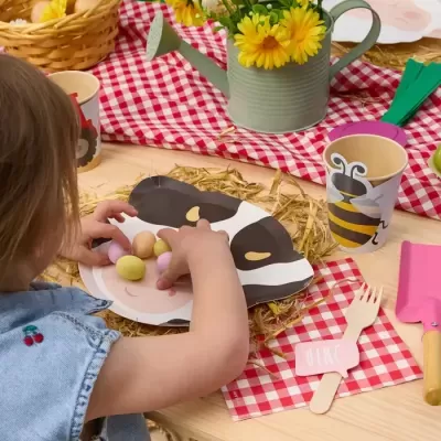 Mesa decorada para festa infantil com prato de vaca, copo de abelha, talheres descartáveis e ovos de chocolate.