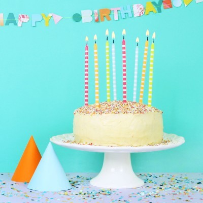 Bolo de aniversário com velas coloridas acesas e decoração festiva num fundo azul