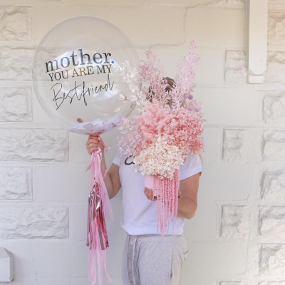 Pessoa segura balão com mensagem e flores secas em tons rosa e branco