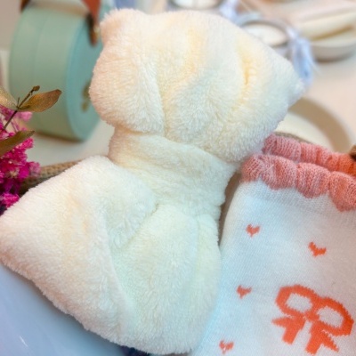 Laço branco felpudo e tecido branco com padrão rosa e laço cor-de-rosa ao lado de flores cor-de-rosa e caixa verde