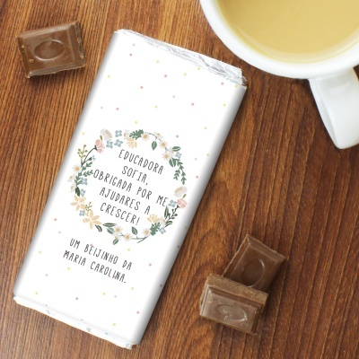 Barra de chocolate embrulhada com mensagem personalizada sobre madeira, pedaços de chocolate e chávena branca