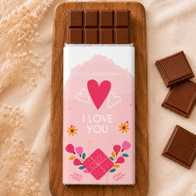 Barra de chocolate com embalagem rosa decorada com corações e flores sobre tábua de madeira.