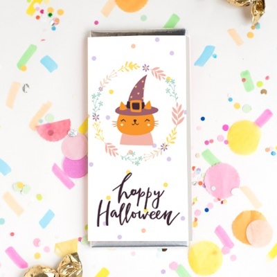 Caixa branca com desenho de gato com chapéu de bruxa e texto 'happy Halloween' rodeada por confetis coloridos