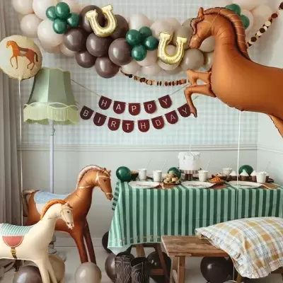 Decoração de aniversário com balões de cavalo, mesa com bolo e toalha verde às riscas