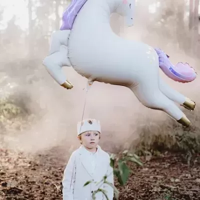Criança com balão de unicórnio branco e roxo em floresta