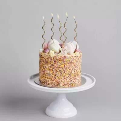 Bolo decorado com granulado colorido e velas espiraladas douradas num suporte branco