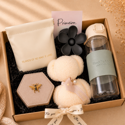 Caixa de presente com garrafa, peluche, broche, bolsa e brinquedo flor num cenário bege