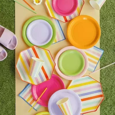 Pratos e copos descartáveis coloridos com riscas multicoloridas em relva artificial