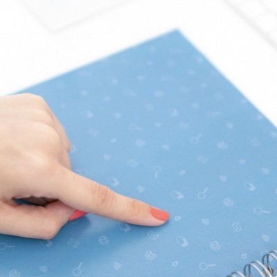 Caderno azul com espiral e mão feminina apontando para a capa