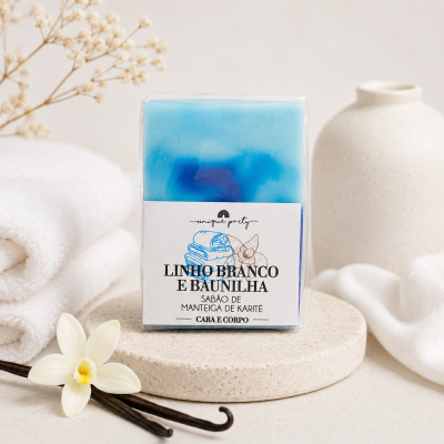 Sabonete azul claro e azul escuro com etiqueta branca e texto, rodeado de toalhas brancas, flor e vagens de baunilha