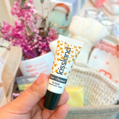 Bálsamo labial Kissland sabor pêssego e coco em tubo branco com corações amarelos