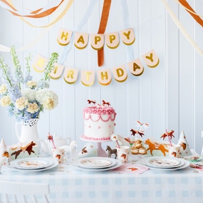 Mesa de aniversário decorada com bolo rosa, decoração de cavalos e faixa 'HAPPY BIRTHDAY'
