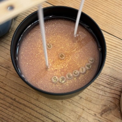 Vela dourada brilhante numa caixa preta redonda com letras feitas de pérolas