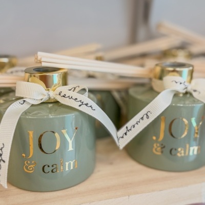 Difusores de aroma verde com tampa dourada e laço branco, com texto dourado JOY & calm