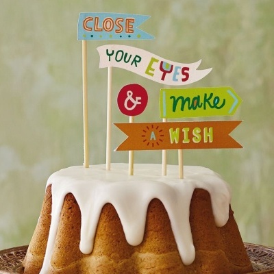 Bolo com cobertura branca e decorações de papel coloridas com texto