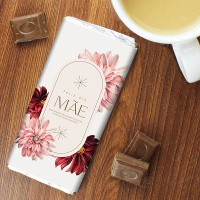Tablete de chocolate com embalagem decorada e texto para o Dia da Mãe, pedaços de chocolate e chávena de café sobre mesa de madeira