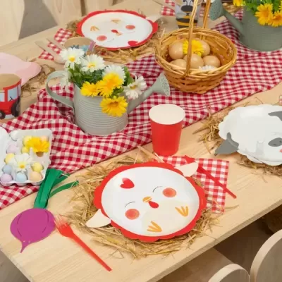 Mesa decorada para festa infantil com pratos de papel, ovos, flores em regadores e toalha vermelha xadrez