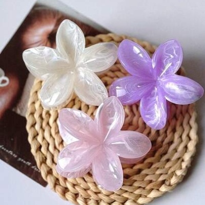 Três presilhas de cabelo florais translúcidas em branco, lilás e rosa sobre base redonda trançada bege