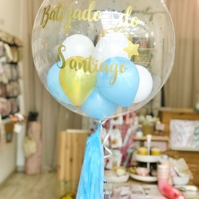 Balão transparente com bolas interiores azuis, brancas e douradas com texto 'Batizado do Santiago'