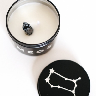 Vela branca numa caixa preta com tampa preta decorada com uma constelação branca.