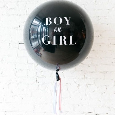 Balão preto com texto branco pendurado com fitas junto a parede de tijolos branca