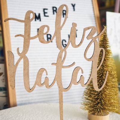 Decoração de mesa de Natal em madeira com texto 'Feliz Natal' e árvore dourada ao fundo