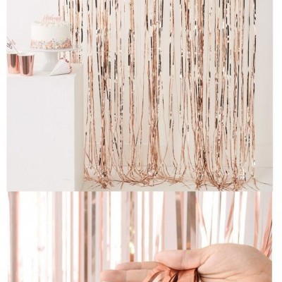 Cortinas decorativas de fita metálica cor de cobre penduradas com bolo e copos ao fundo, e mão a segurar fitas