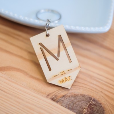 Porta-chaves em madeira clara com letra M e texto DE MÃE sobre mesa de madeira