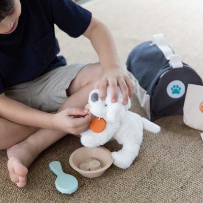 Criança a brincar com cão de peluche branco, tigela e escova azul claro, com mala preta ao fundo