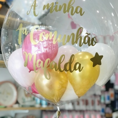 Balão transparente com balões interiores coloridos e texto dourado para uma festa de comunhão