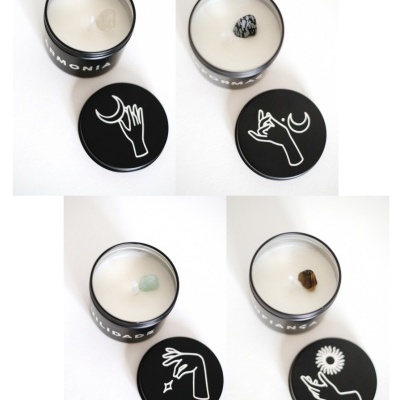Quatro velas em recipientes negros com pedras e tampas decoradas com mãos e símbolos