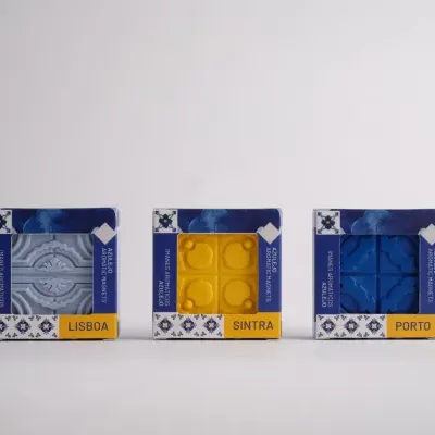 Imanes aromáticos tipo azulejo em caixas com as cores cinza, amarelo e azul etiquetadas como LISBOA, SINTRA e PORTO.