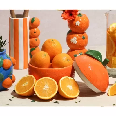 Cerâmicas decorativas com motivos de laranja e frutas frescas sobre mesa clara
